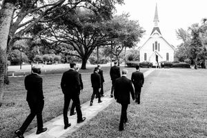 A black and white photo of a group walking towards a white chapel across a grassy lawn.