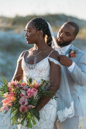 A romantic wedding portrait on the beach featuring newlyweds with a vibrant coral and pink bouquet.