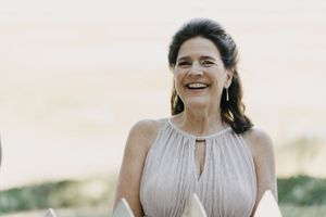 A woman in a light beige halter dress laughs joyfully against a soft sunset background.