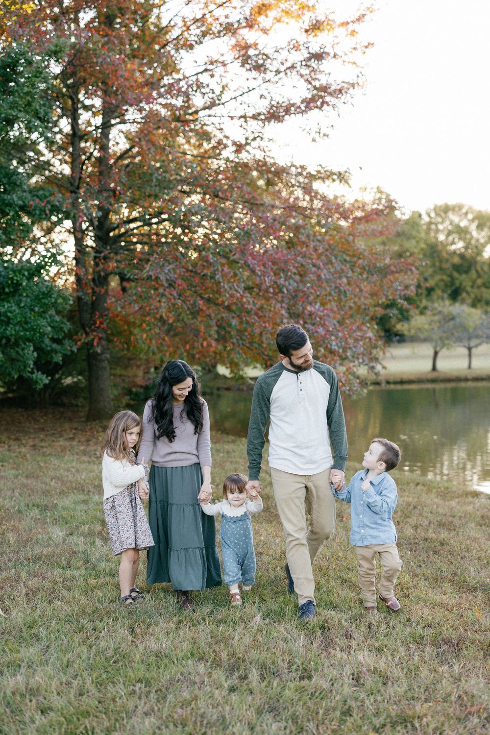 A group walks together on grassy hill near a lake during autumn with trees showing fall colors in the background.