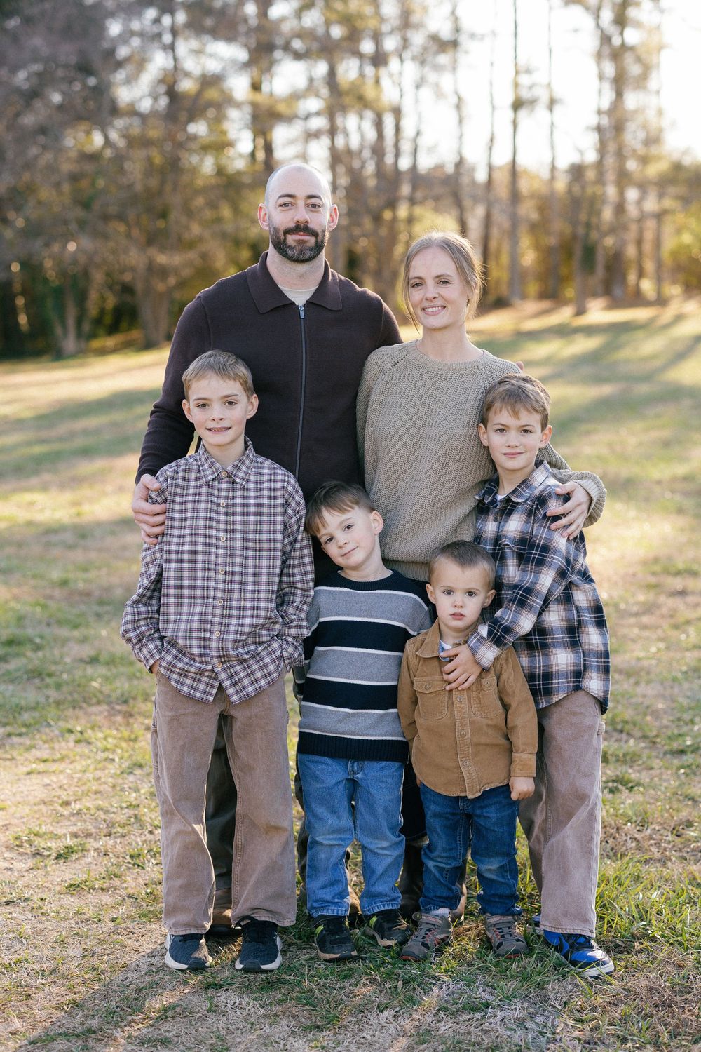 A family of four poses together outdoors on a grassy hillside during golden hour.