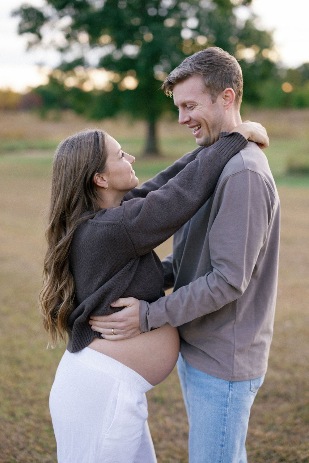 A couple embraces and laughs together in a grassy field during golden hour.
