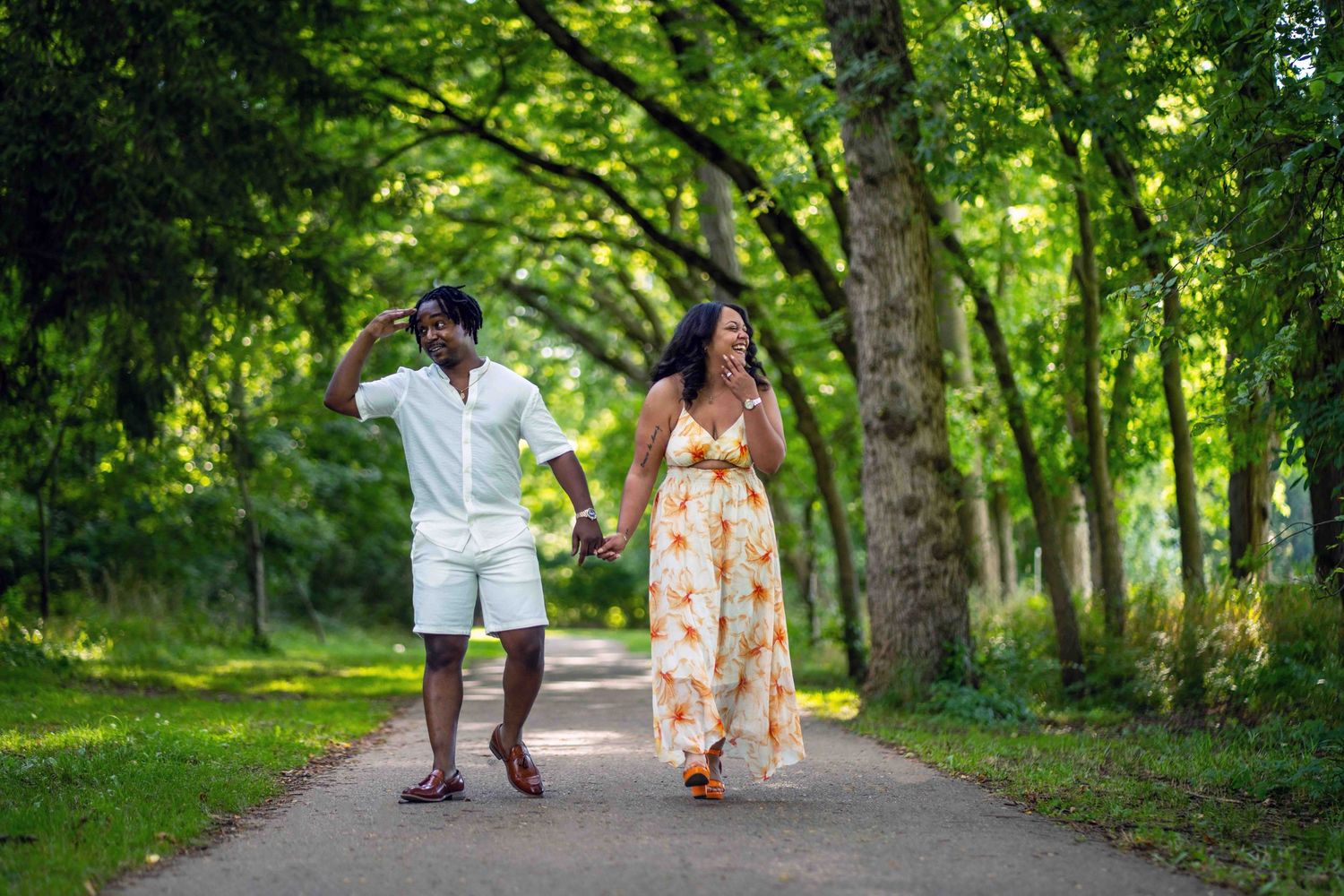 engaged couple walk together on a tree-lined path surrounded by lush green foliage for their photo session