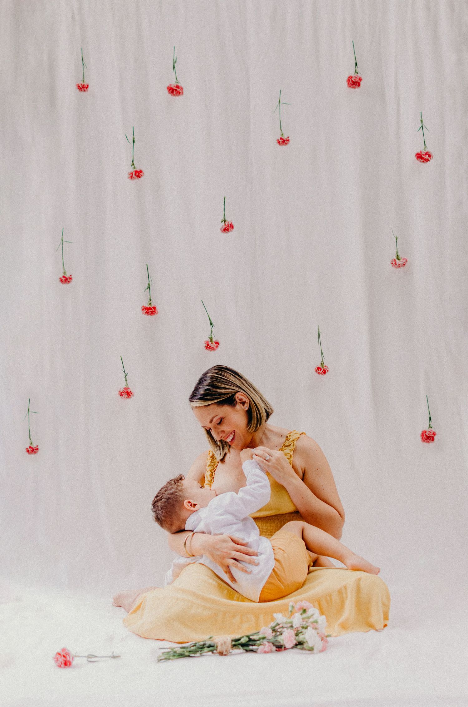 Sweet maternal moment against white backdrop with delicate hanging red flower decorations.