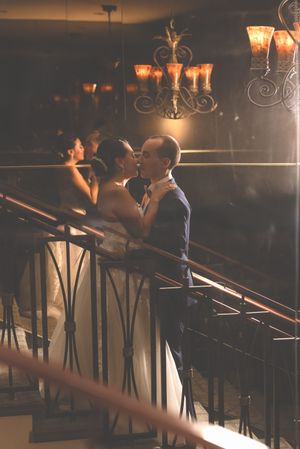 Wedding couple sharing an intimate moment at a dimly lit venue with decorative lighting and railings.