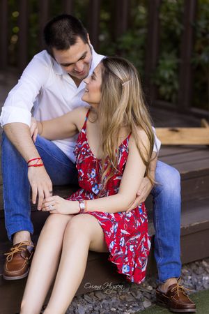 Couple sharing a romantic moment sitting on steps, woman in red floral dress and man in white shirt and jeans.