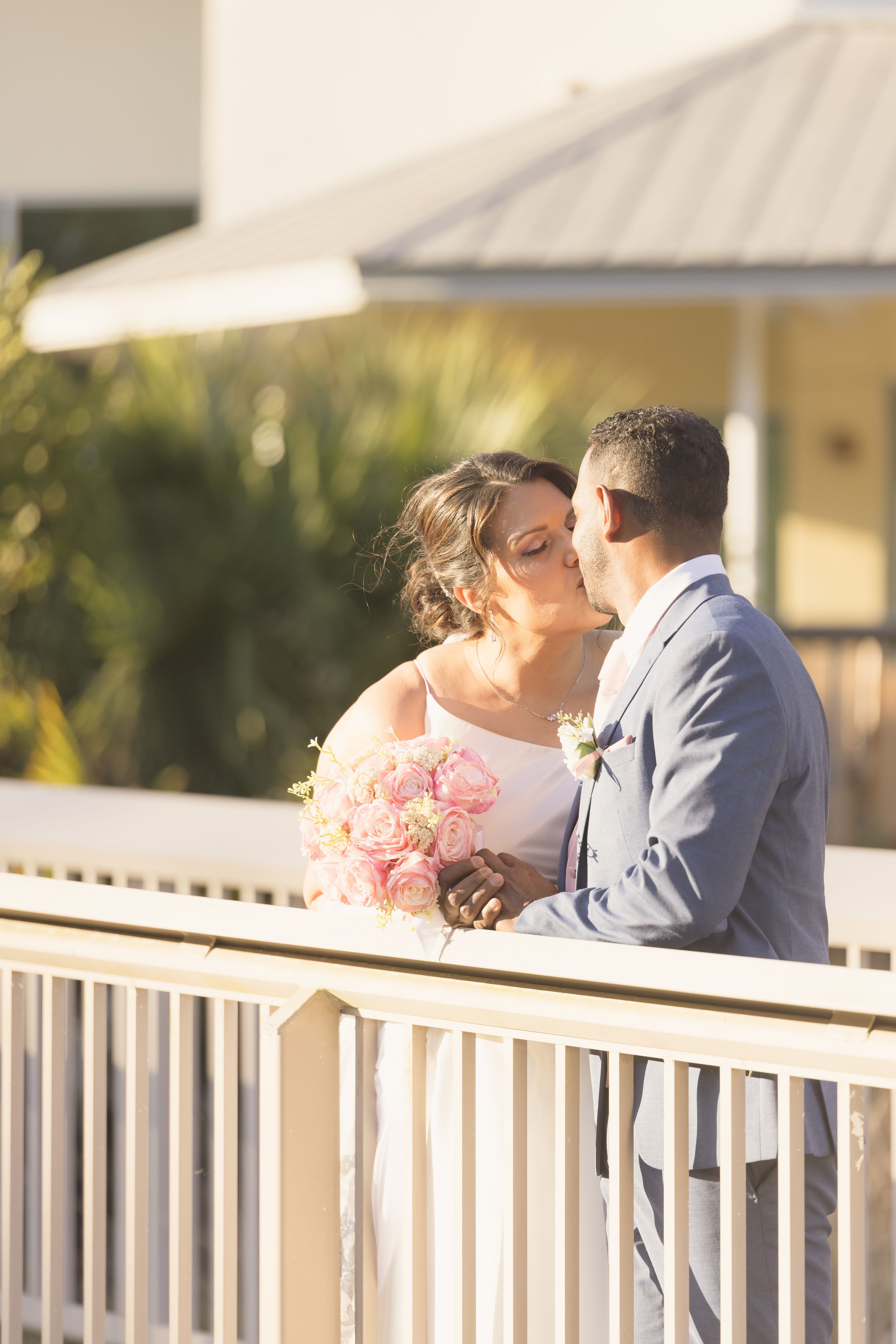 Two people share an intimate moment on a white railing balcony during sunset.