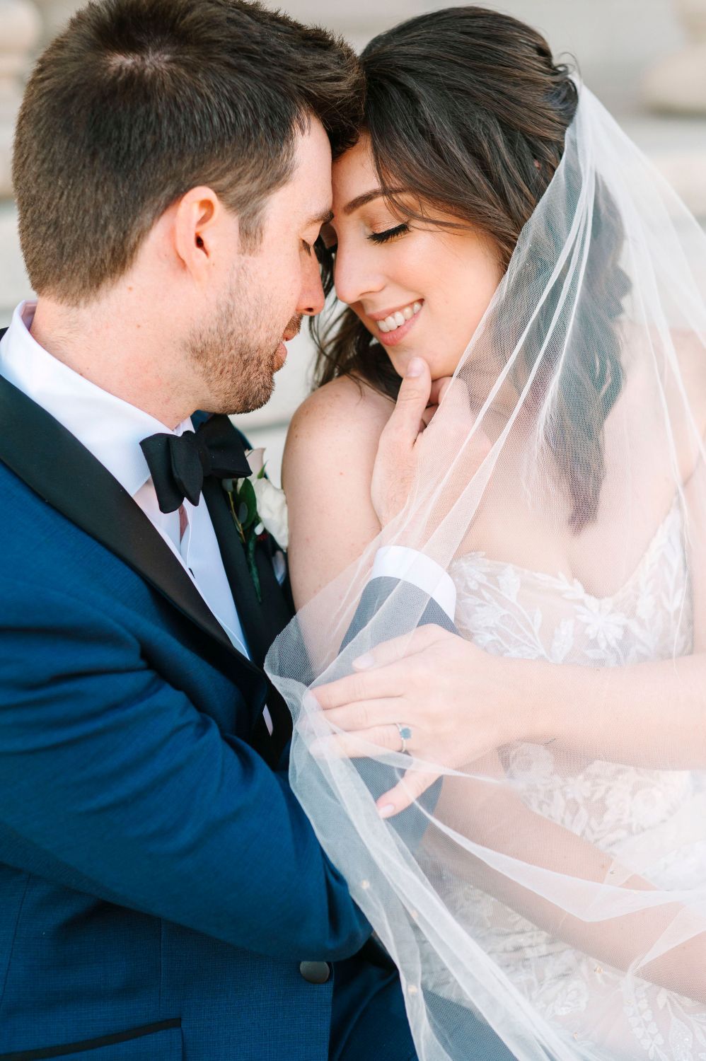 Romantic wedding couple sharing intimate moments under a delicate white veil against a soft background.