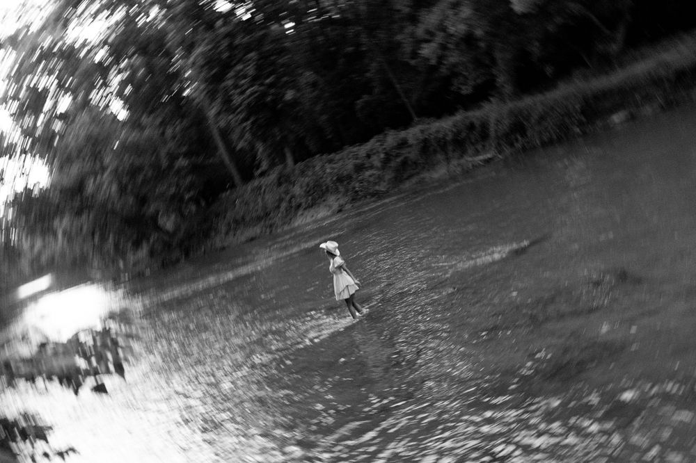 Black and white fisheye photo of a woman in a white dress standing in a river.