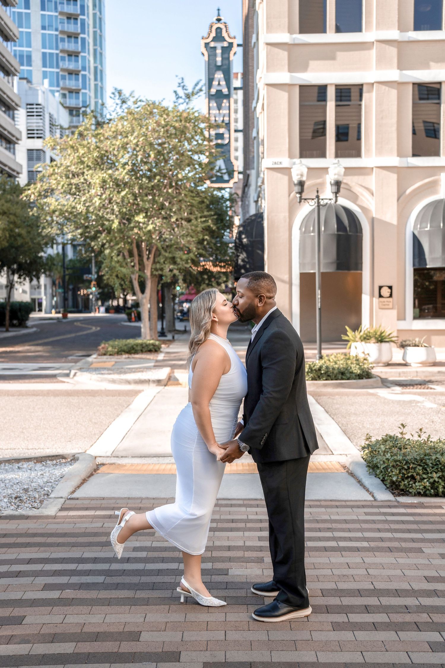 A couple in wedding attire dances playfully on brick pavement with urban buildings in the background in Downtown Tampa