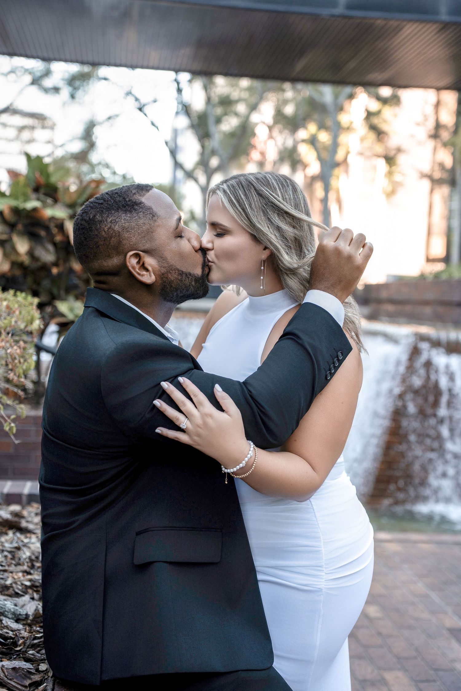 A romantic wedding couple shares an intimate kiss in front of a waterfall backdrop in Downtown Tampa