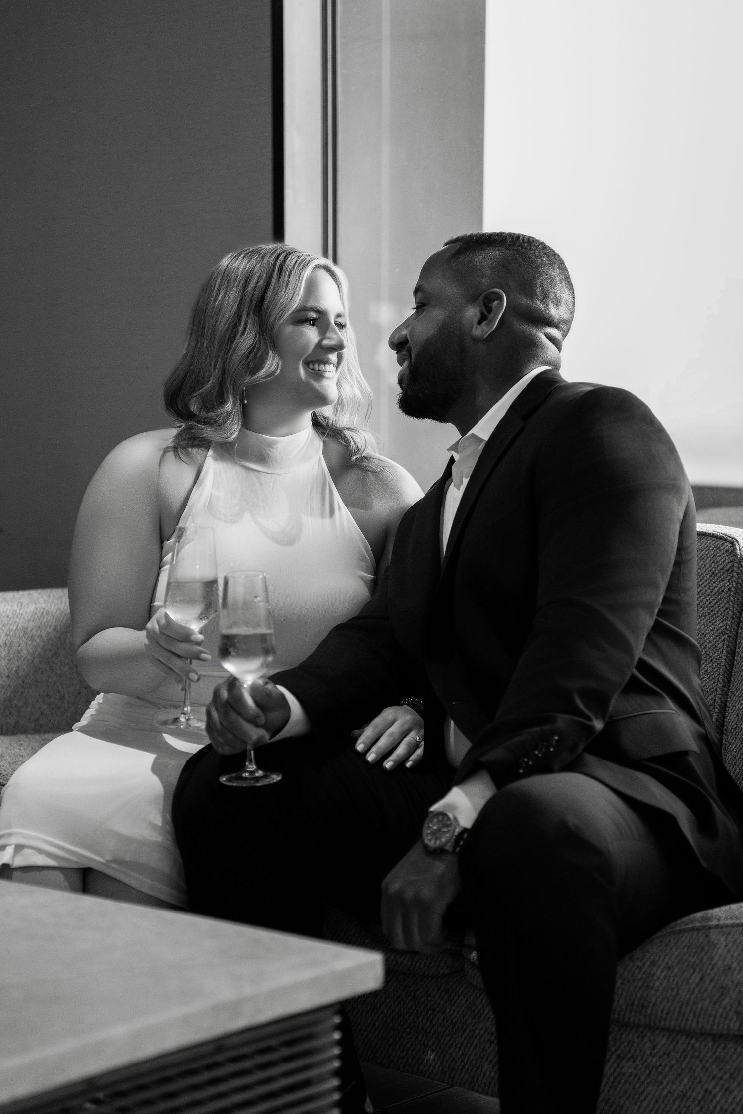 A couple in formal wear shares romantic moments on a couch while holding wine glasses in Downtown Tampa