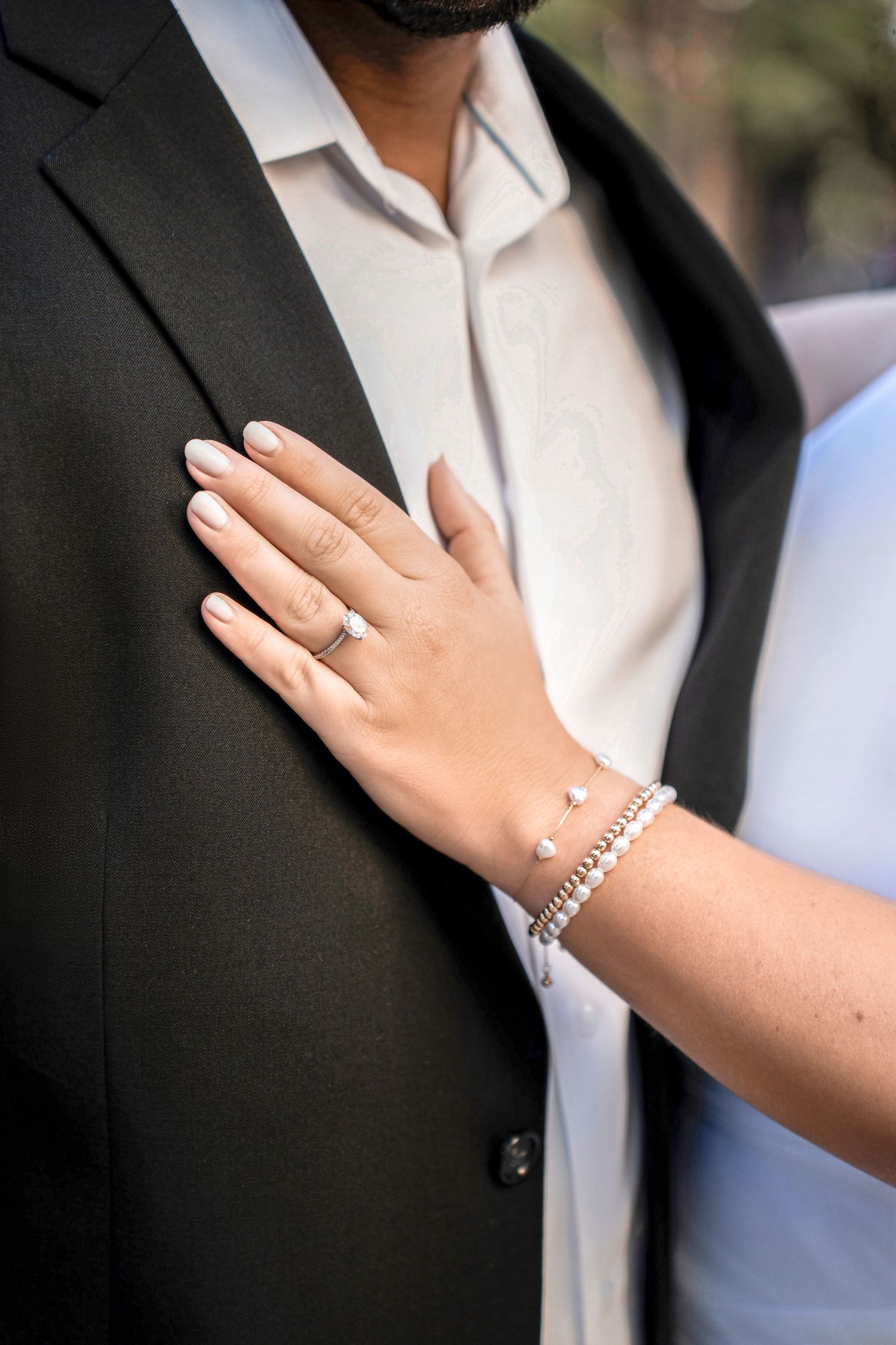 A hand wearing an engagement ring and bracelet rests on a black suit jacket over a white shirt in Downtown Tampa