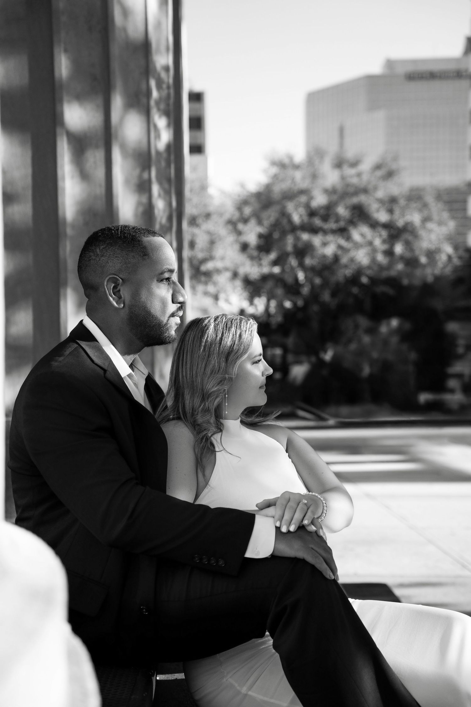 A romantic black and white photo series showing a couple embracing while seated on an outdoor bench in Downtown Tampa