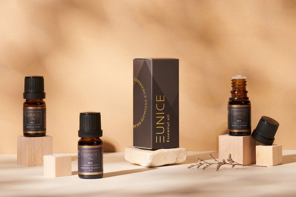 Essential oil bottles and product packaging arranged on beige blocks in warm lighting with minimalist styling.