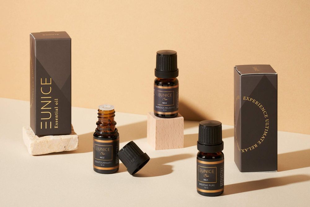 Small dark glass bottles and product boxes cast dramatic shadows on a beige surface in a minimalist beauty product layout.