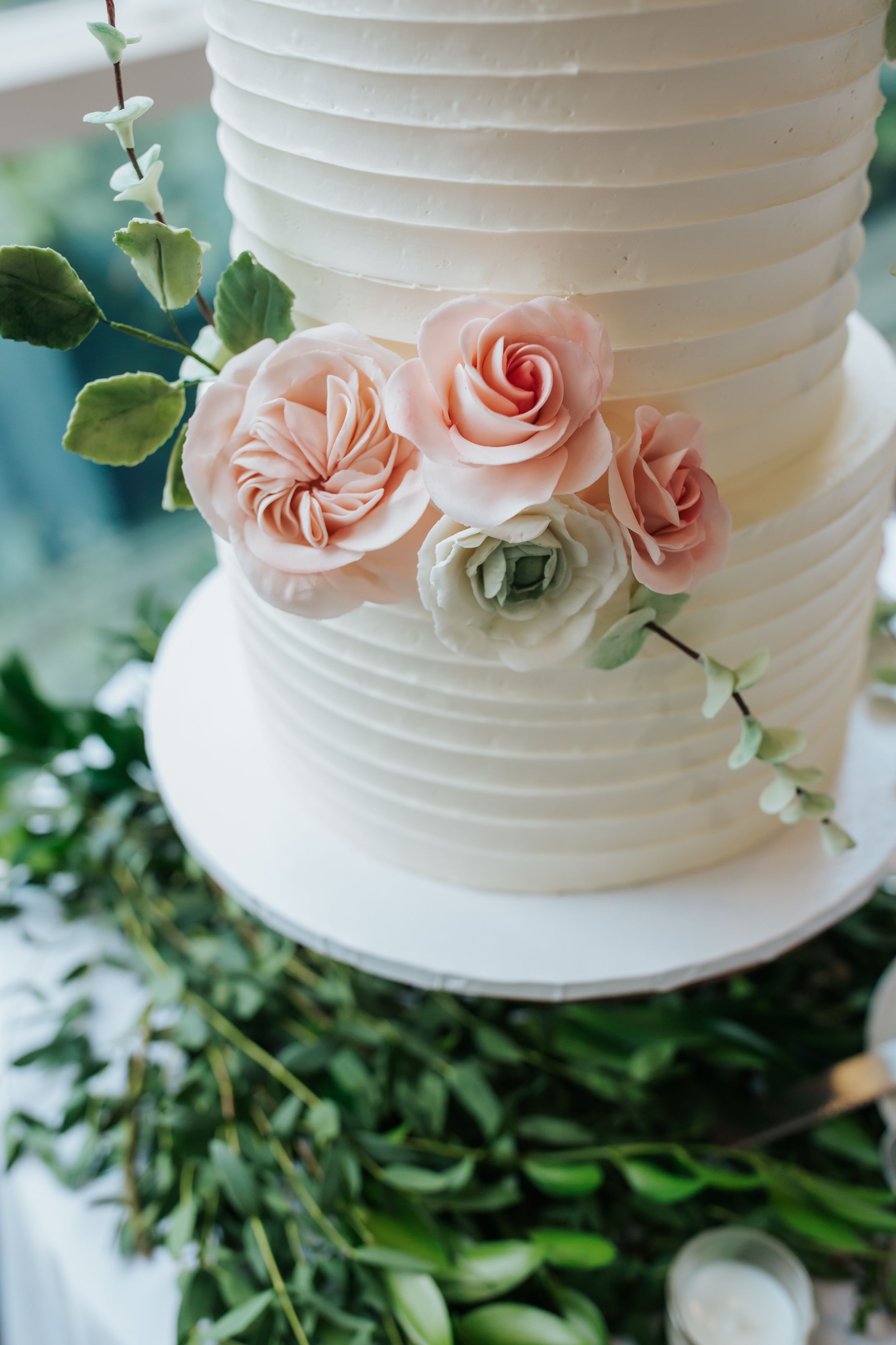 Close-up view of an elegant white wedding cake with delicate horizontal ribbing and soft pink roses as decoration.