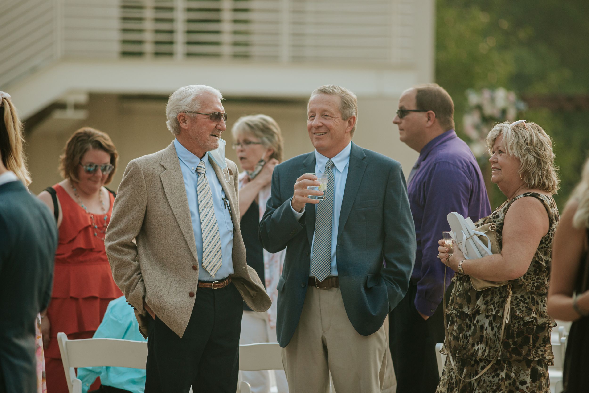 A group of guests mingling and socializing at an outdoor event with drinks in their hands.