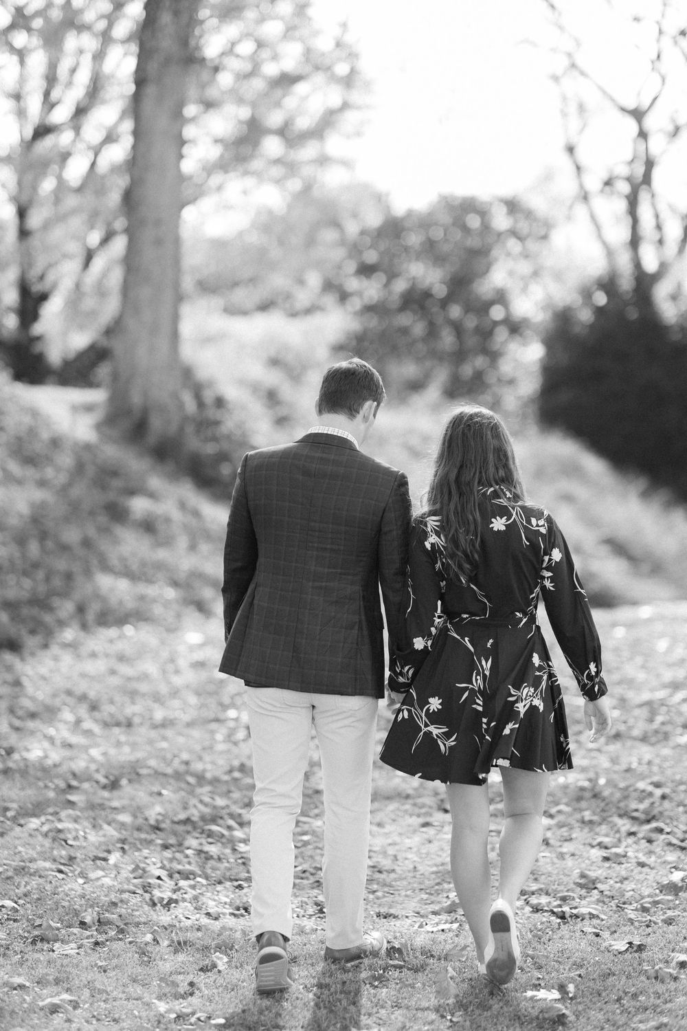 Black and white photo of couple walking away together on autumn path.