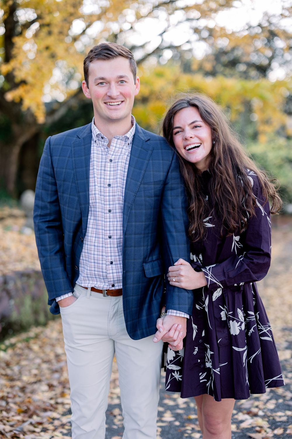 Joyful couple laughs together during autumn photoshoot in park.