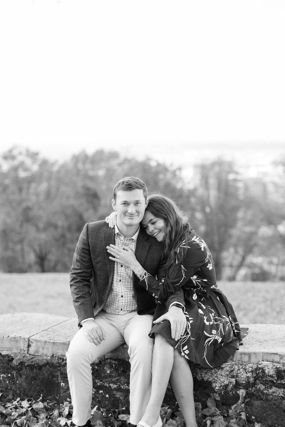 Black and white portrait of couple sitting together on stone wall outdoors.