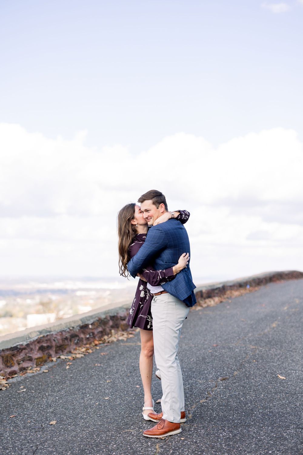 Romantic couple embracing on hilltop path with cloudy sky background.