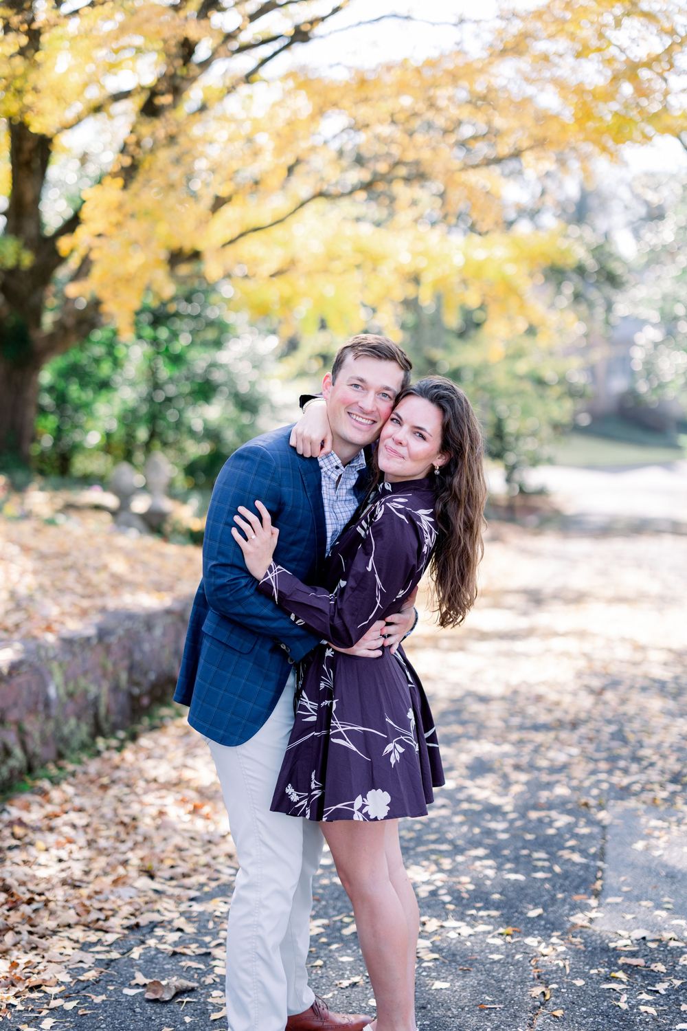Romantic autumn engagement photo with couple embracing under yellow fall foliage.