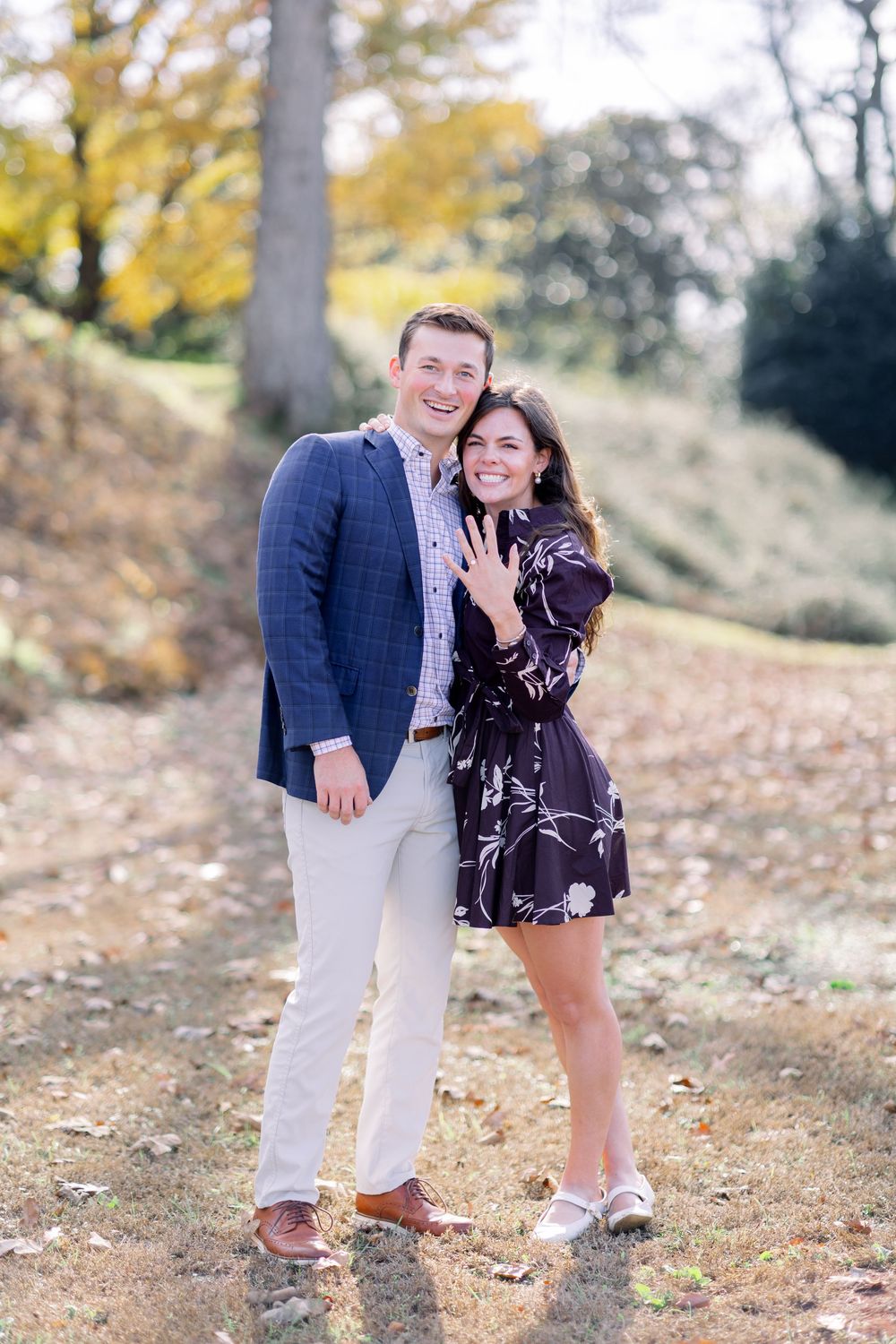 Happy couple poses together on fall day showing off engagement ring.