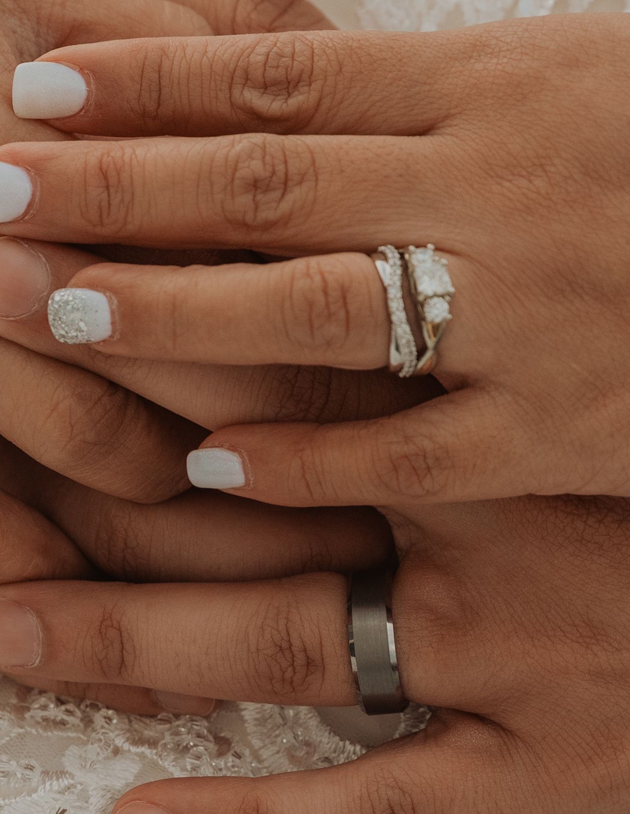 Close-up of bride and groom hands showing diamond engagement ring and wedding bands.