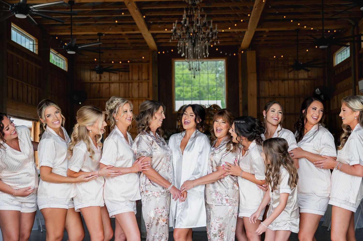 Group wearing matching white robes celebrating in rustic wooden venue with string lights.