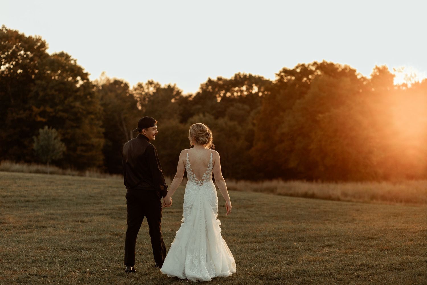 Silhouette of newlyweds walking in a field at sunset with dramatic golden lighting.