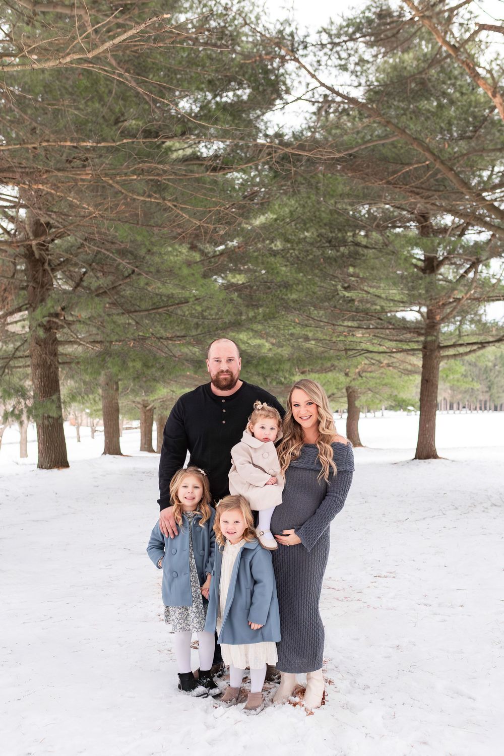 A winter photo session in a snowy pine forest with evergreen trees creating a serene white backdrop.