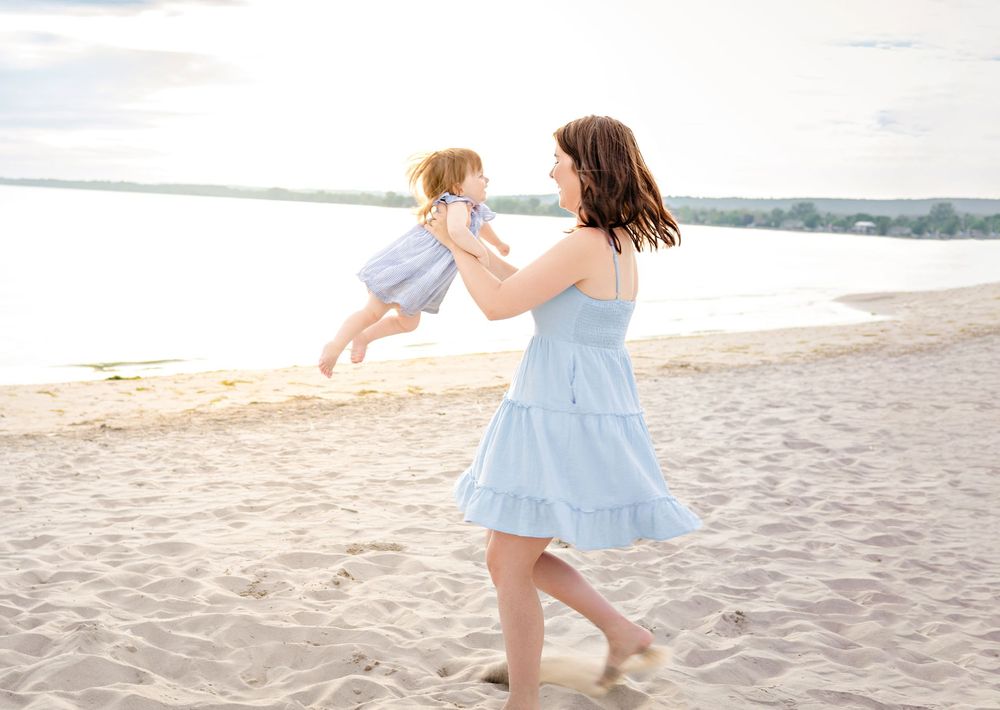 Two people in light blue dresses dance and twirl together on a sandy beach at sunset.