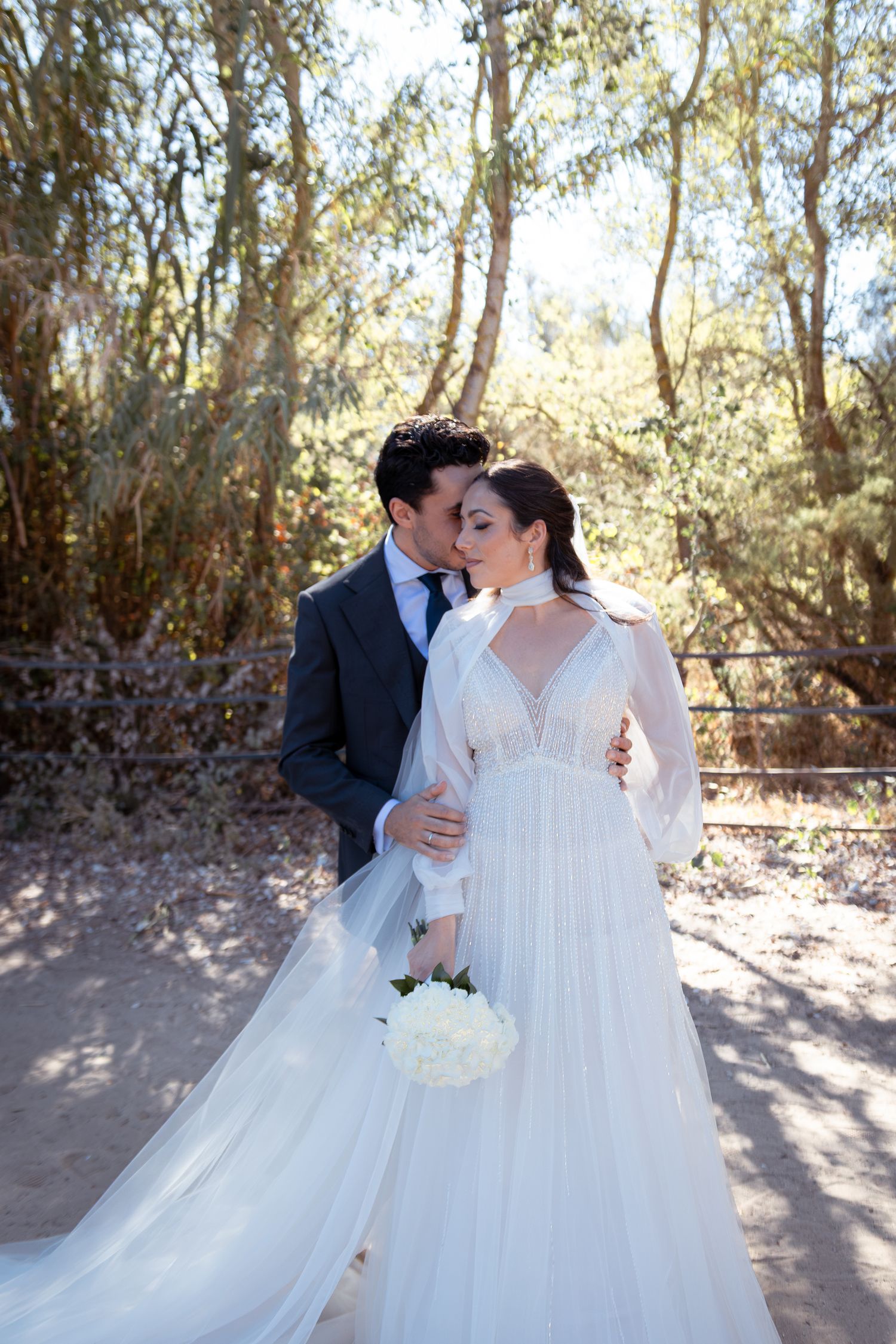 A couple shares a romantic dance in the snow while wearing formal wedding attire with a flowing white dress.