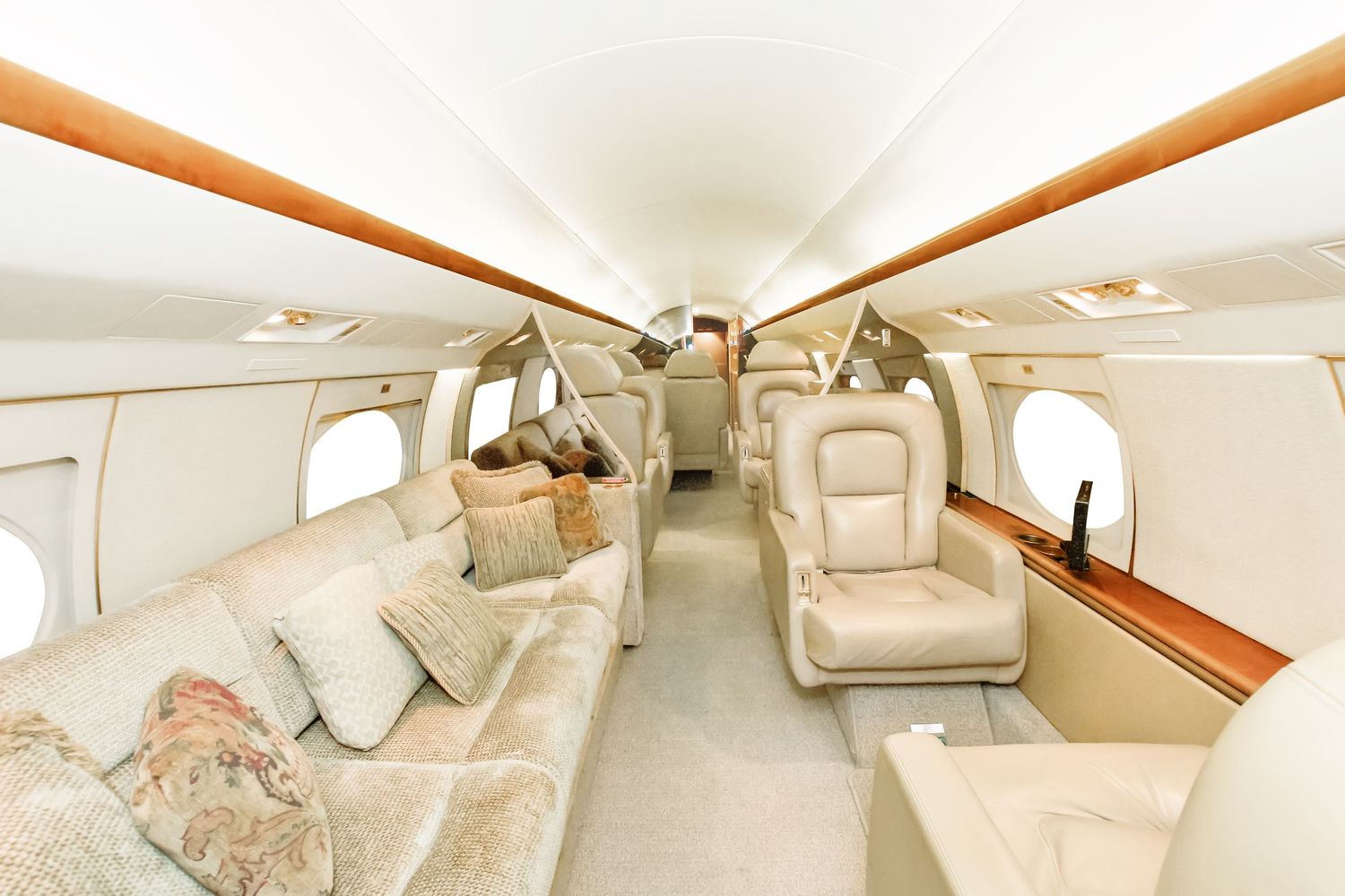 Luxurious private jet interior showing plush beige leather seating and wood trim details.