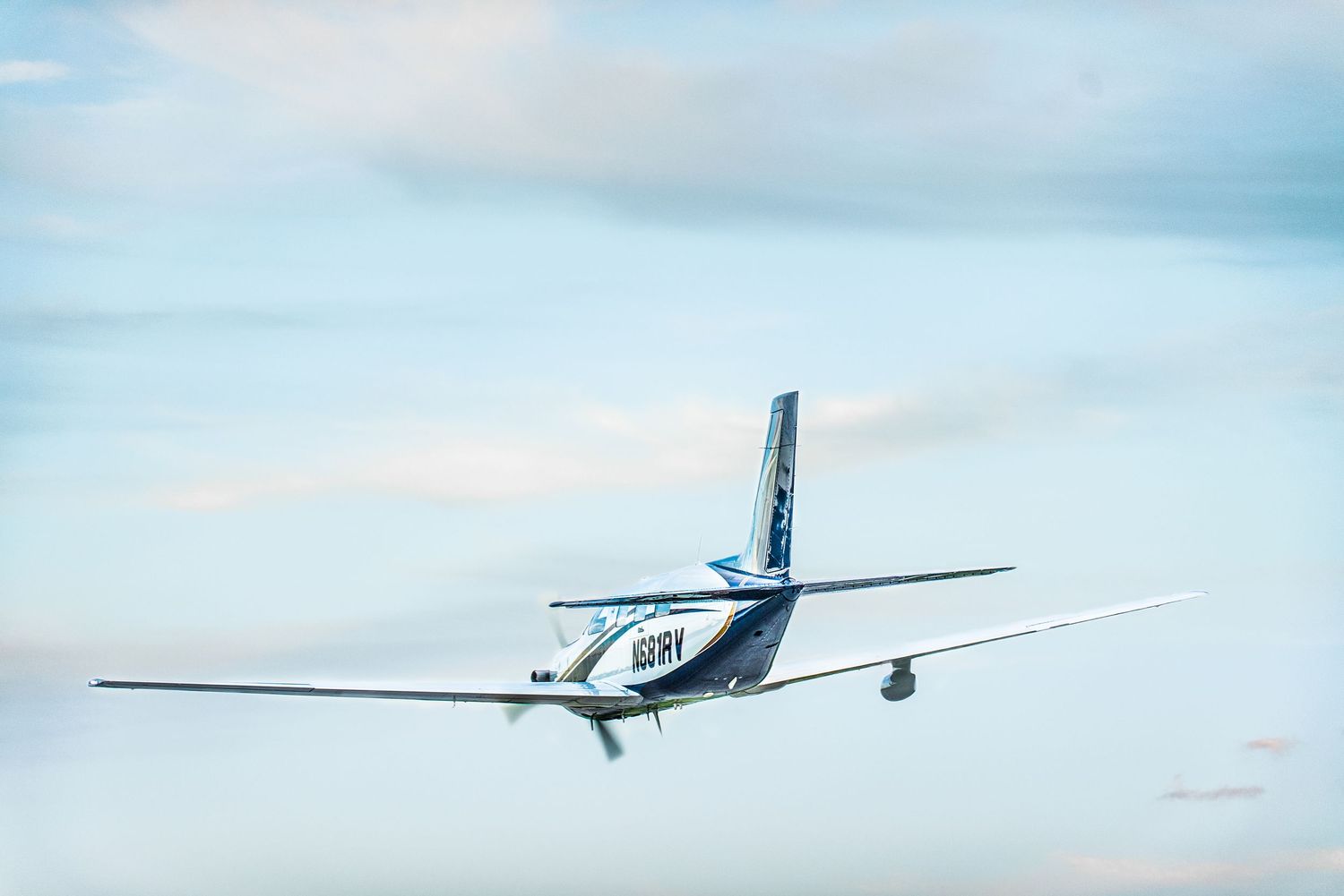 Small white private aircraft flying against blue sky with scattered clouds.