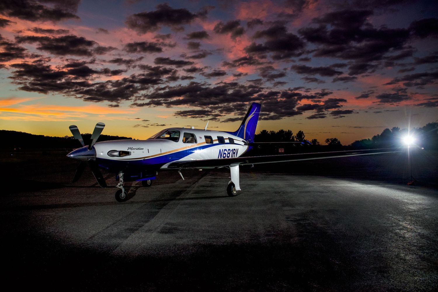 Private jet silhouetted against dramatic purple and orange sunset sky on airport tarmac.