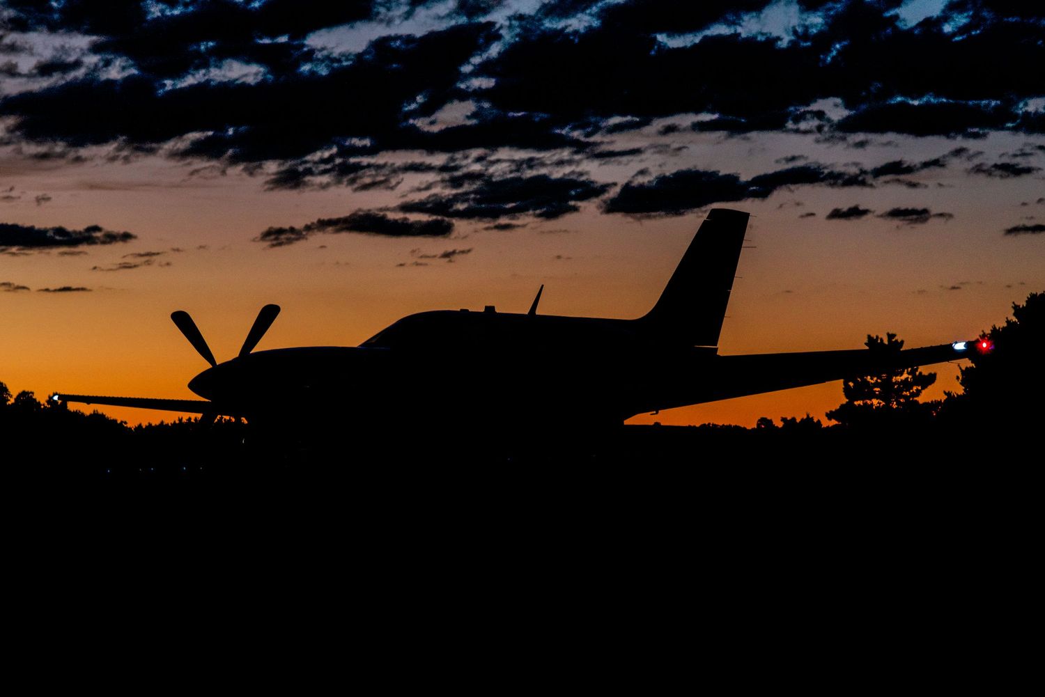 Silhouette of a small aircraft flying against a vibrant orange and purple sunset sky with dark clouds.