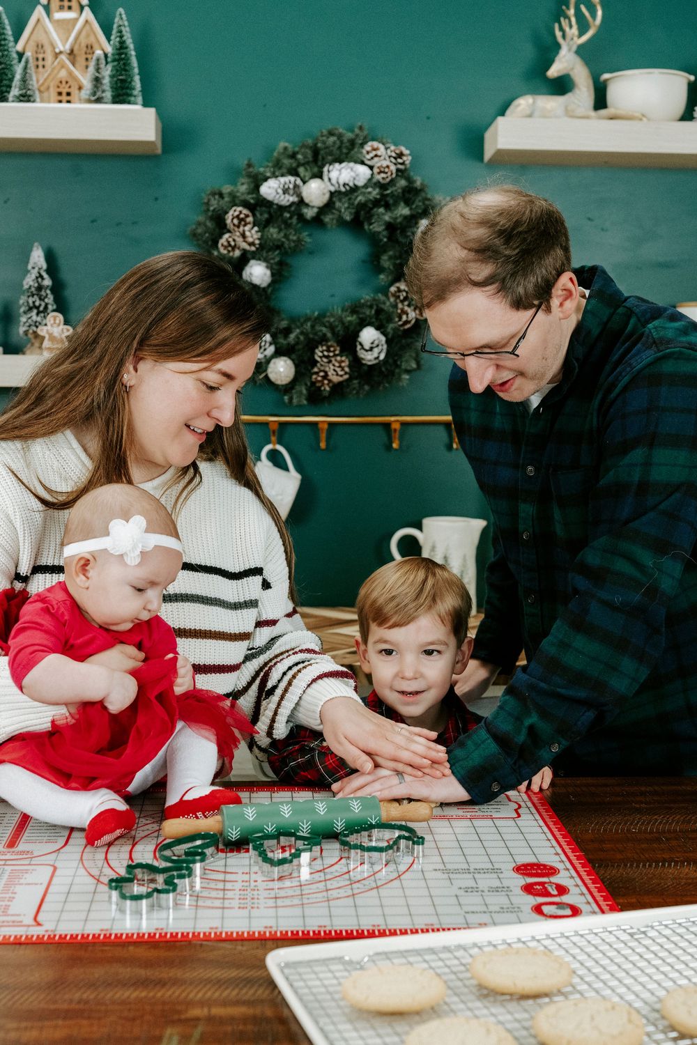 Family baking together in kitchen with red and white checkered tablecloth and teal wall in background.