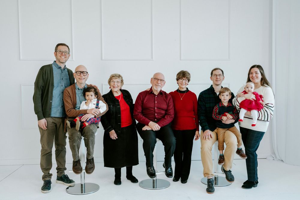Multi-generational family group wearing red and casual attire poses together against white studio backdrop.