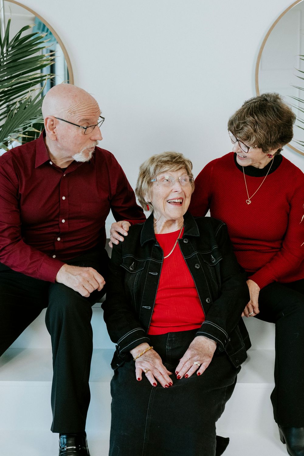 An elderly couple wearing red and black outfits share joyful laughter while sitting together in a bright studio setting.