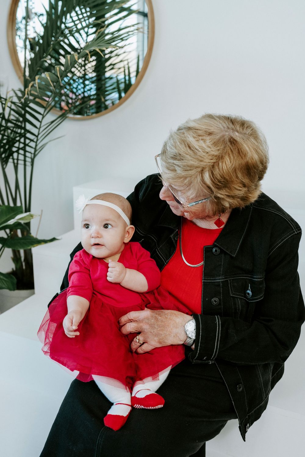 A series of candid moments showing a baby in a red dress being held and interacting with someone in black attire.