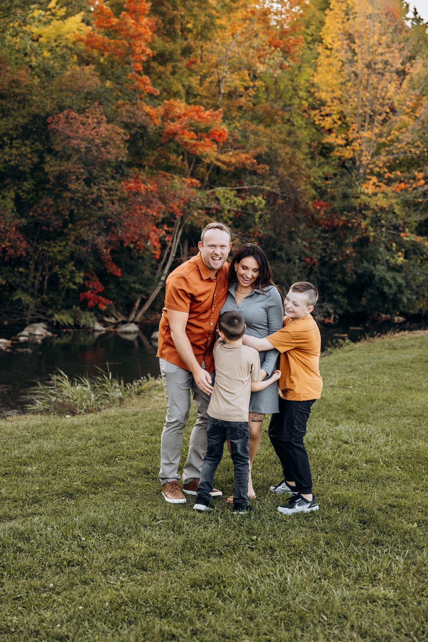 A family enjoys an autumn day together by a pond surrounded by colorful fall foliage and trees.