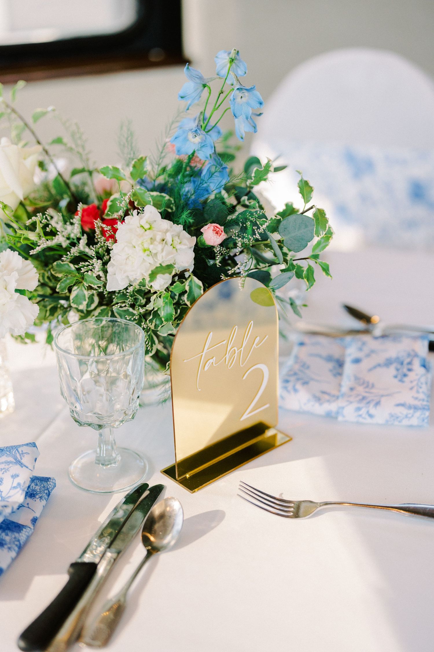 Elegant wedding table setting with delicate blue flowers and gold table numbers in glass vases.