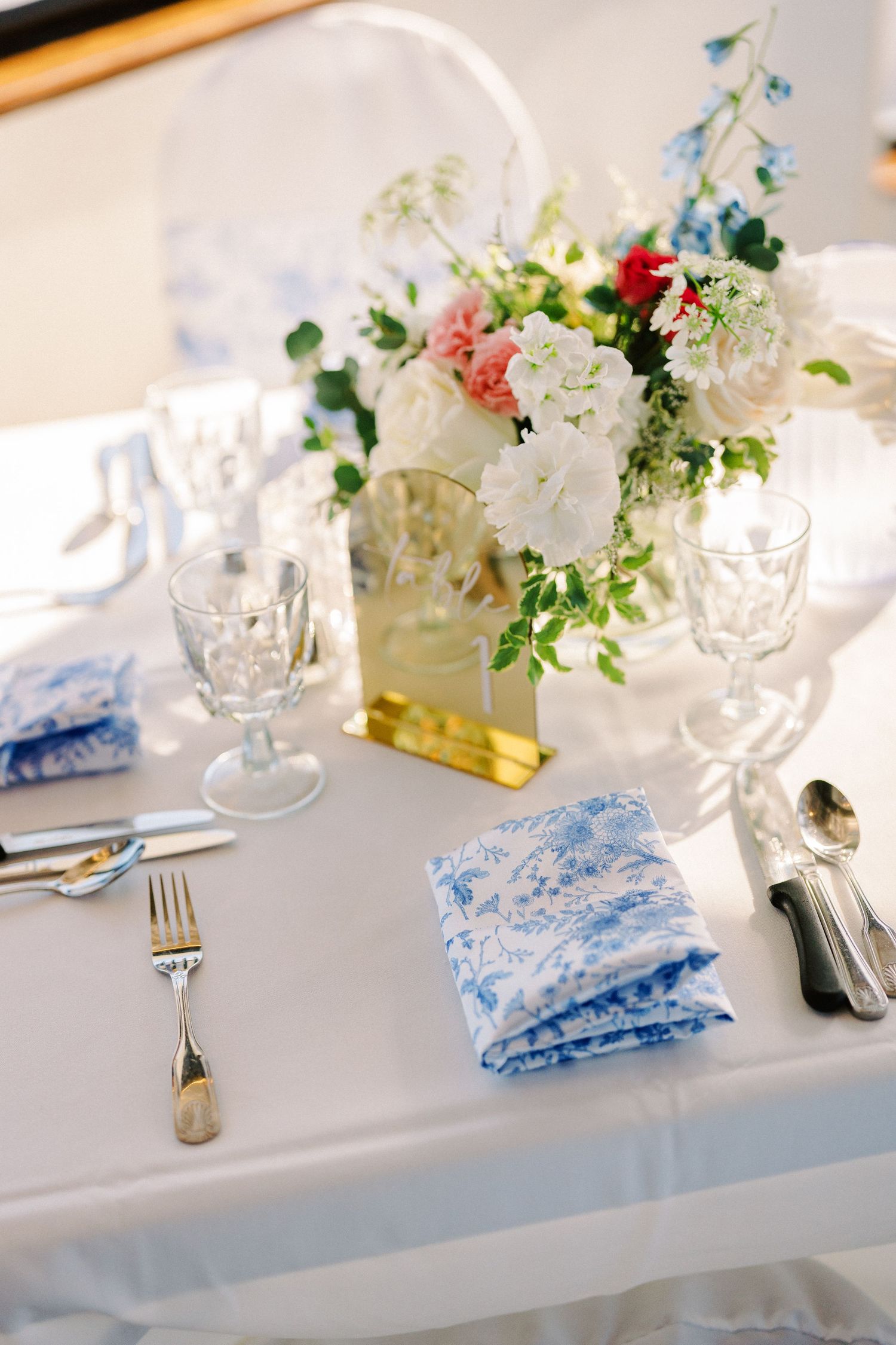Elegant table setting with white and pink floral centerpiece, crystal glasses, and blue patterned napkins on white tablecloth.