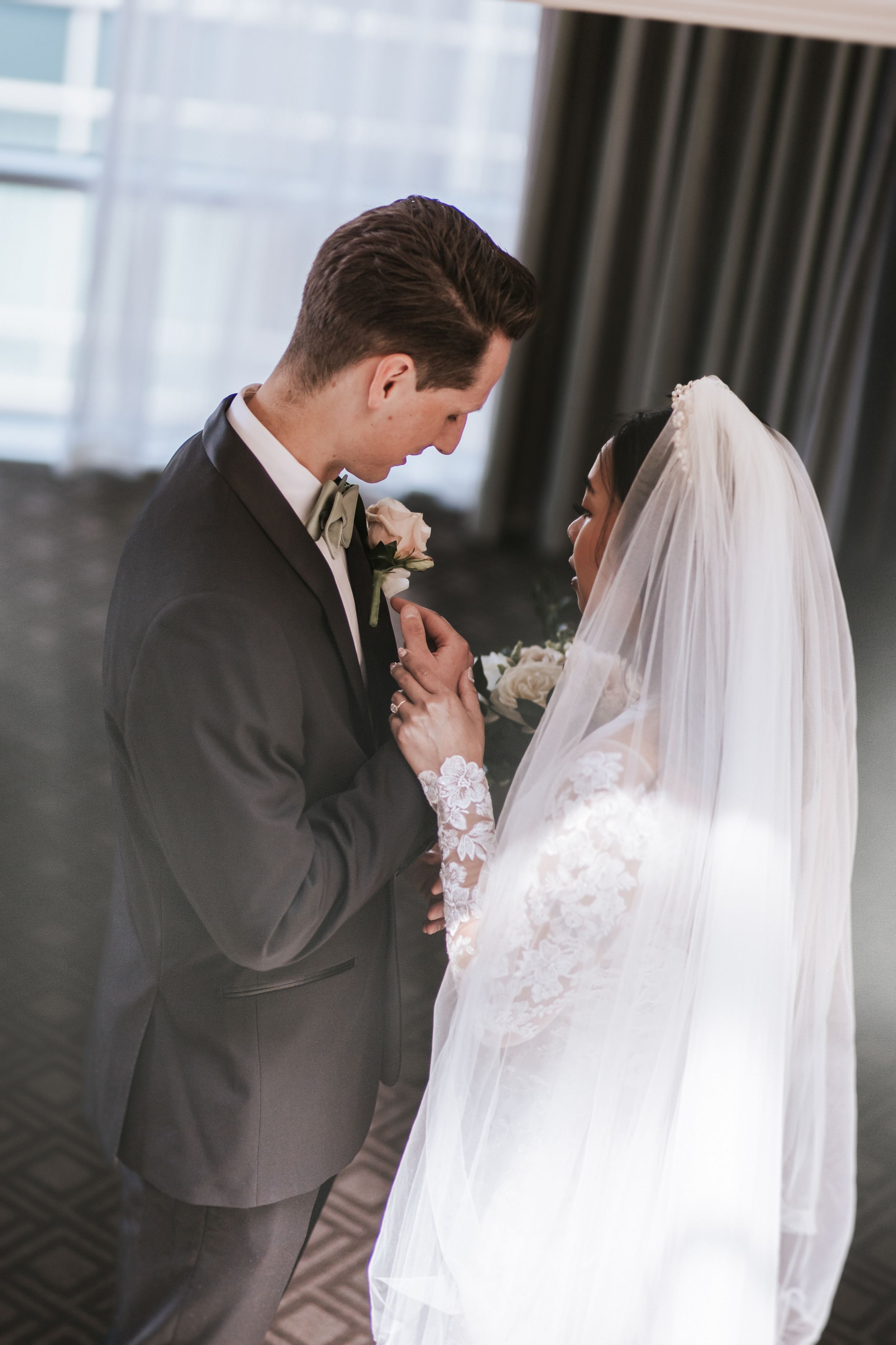 Emotional first look between bride and groom at wedding ceremony with flowing white veil and dark suit.