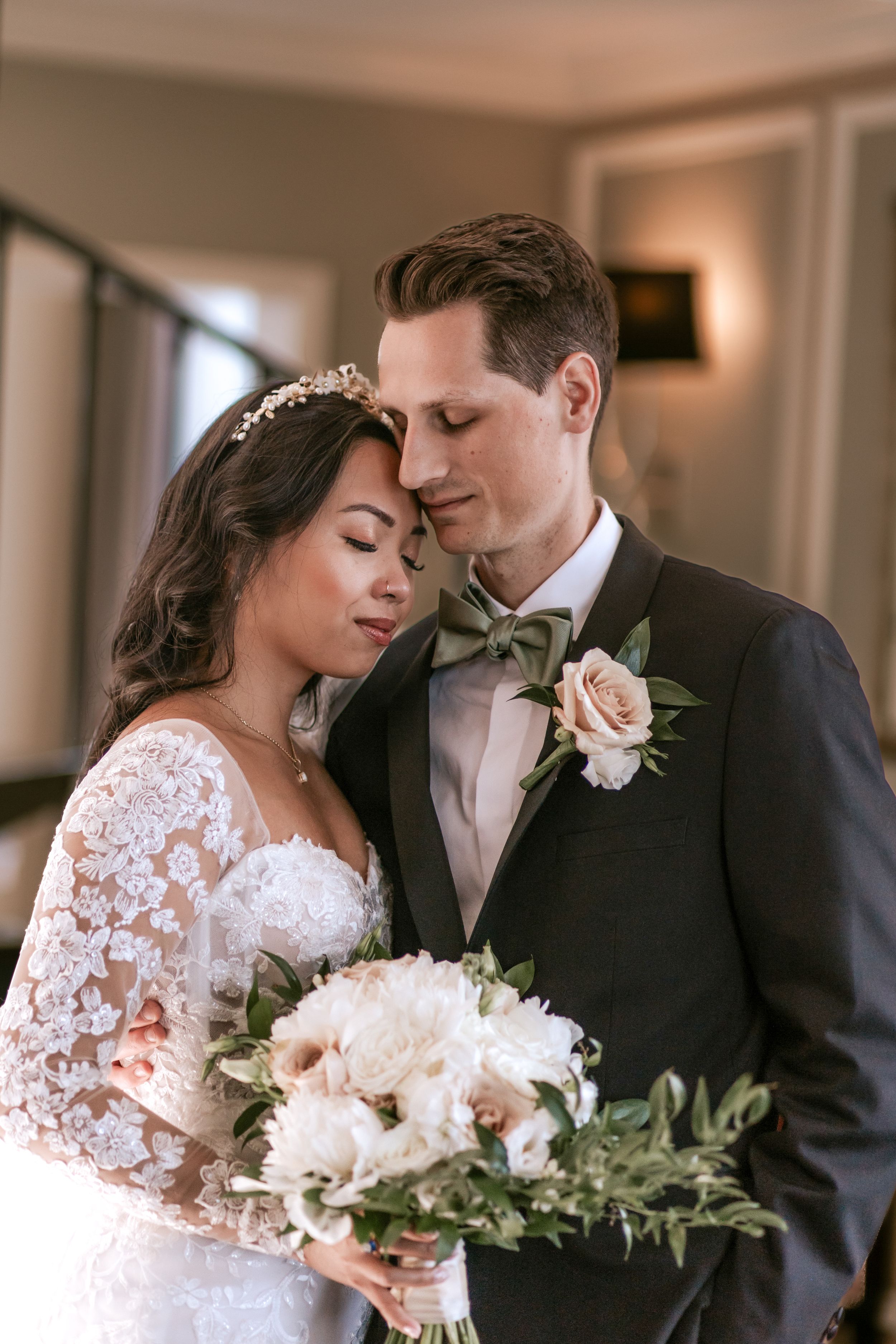 A romantic wedding moment with a couple embracing while holding a blush pink and white floral bouquet with greenery.