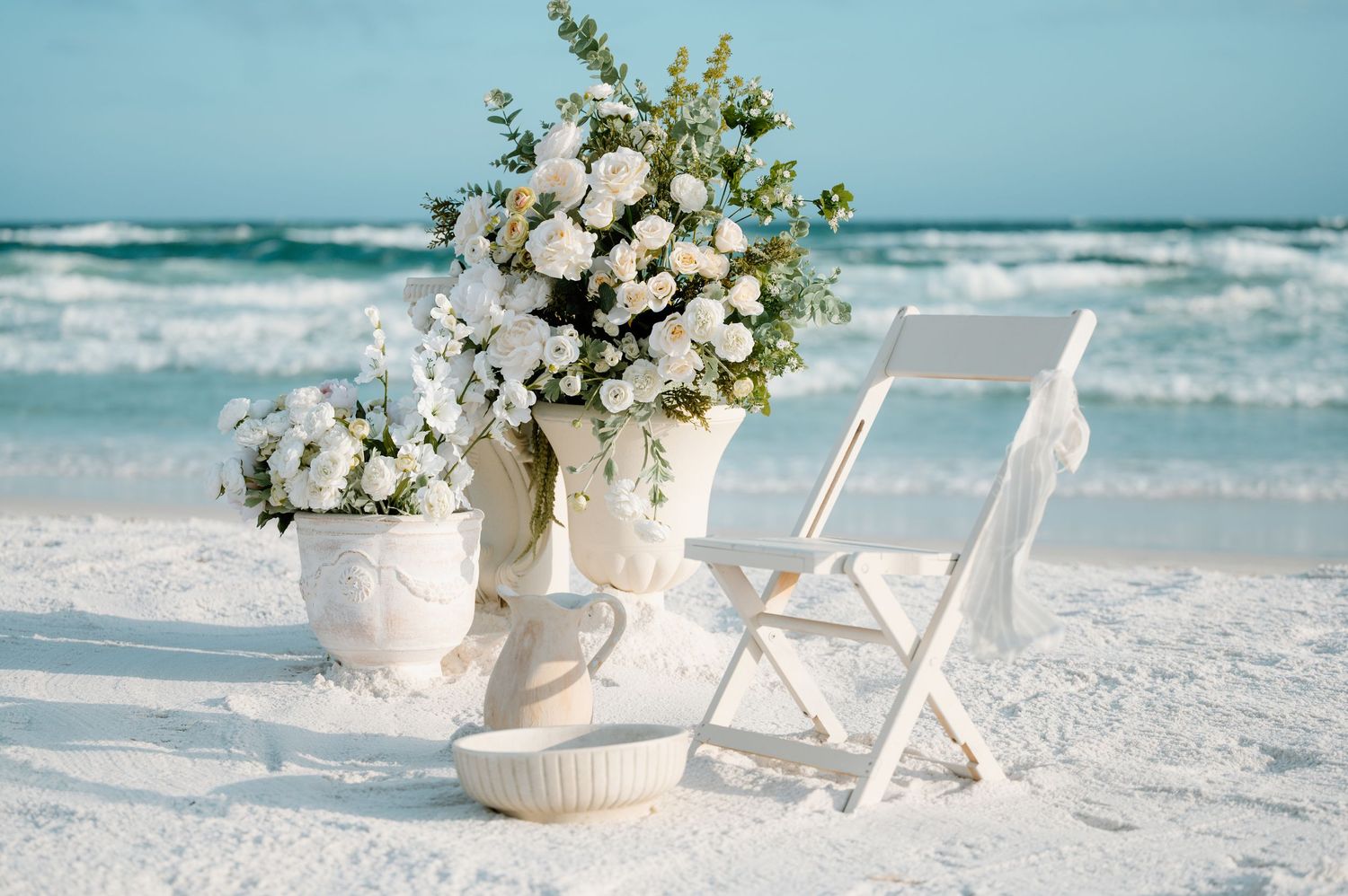 A couple in wedding attire embraces romantically on a beach at sunset with waves crashing around them.