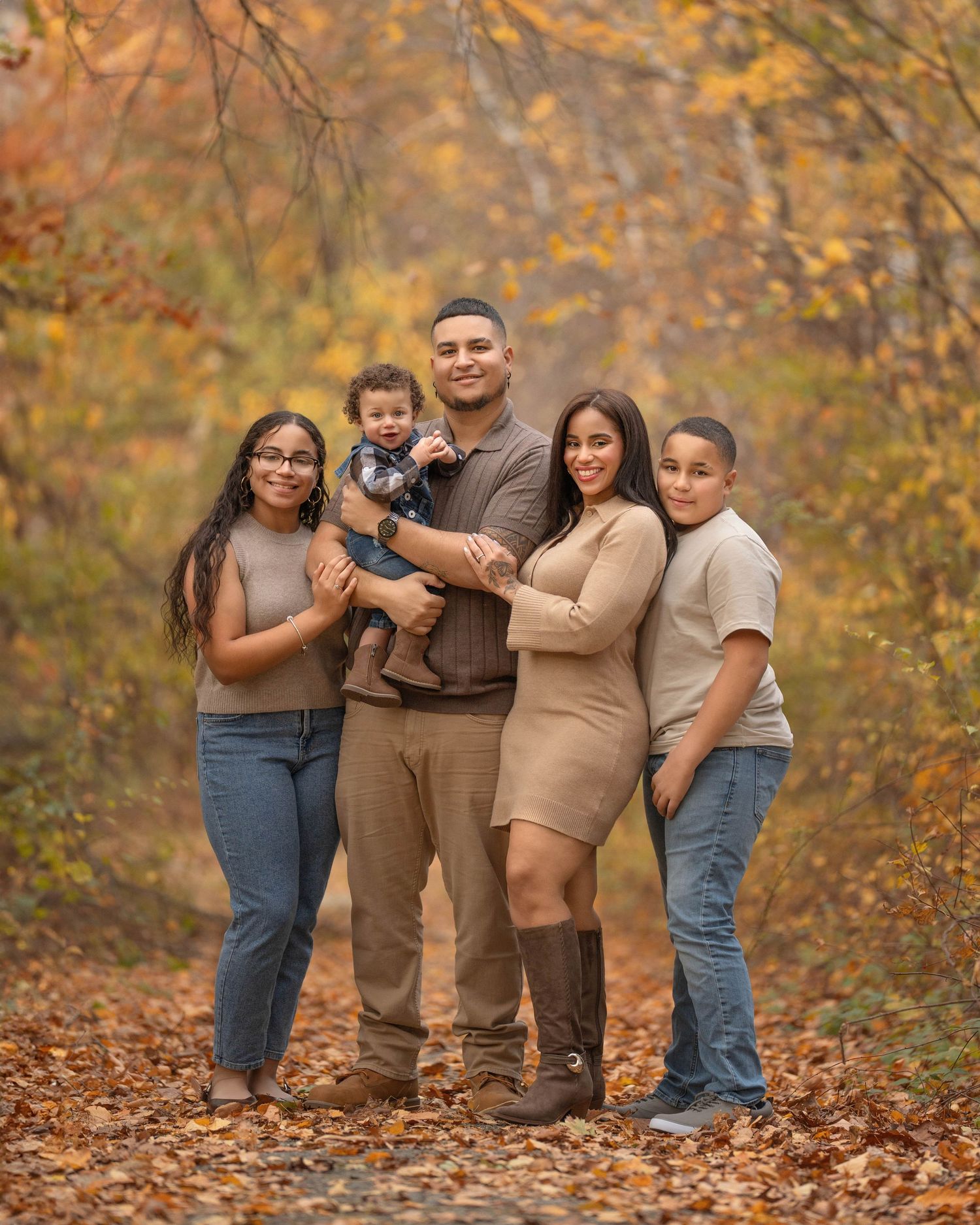 A group poses together outdoors in coordinated brown and beige outfits against a backdrop of autumn foliage.