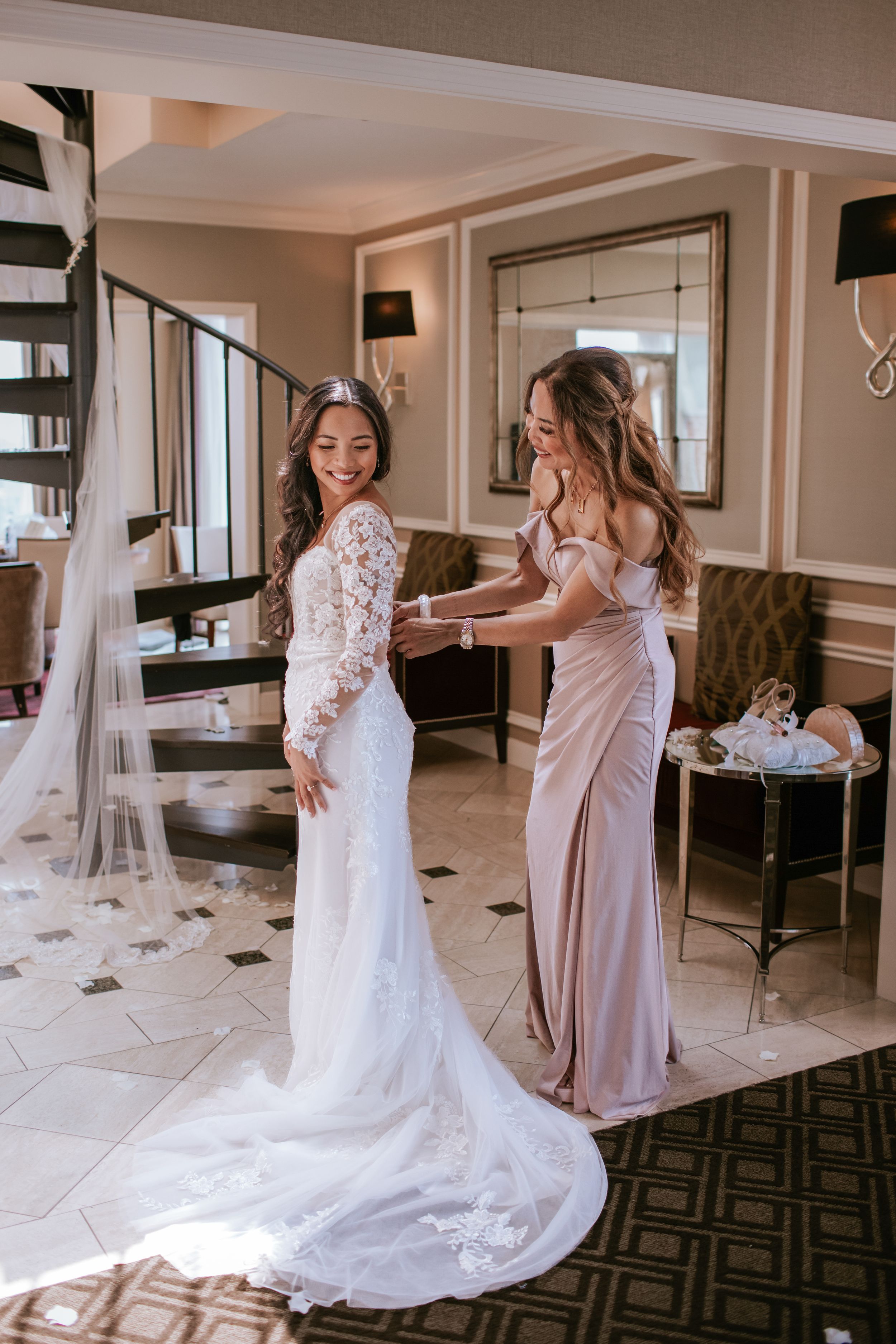 Bride getting ready with bridesmaids in hotel suite wearing blush pink dresses and white lace wedding gown.